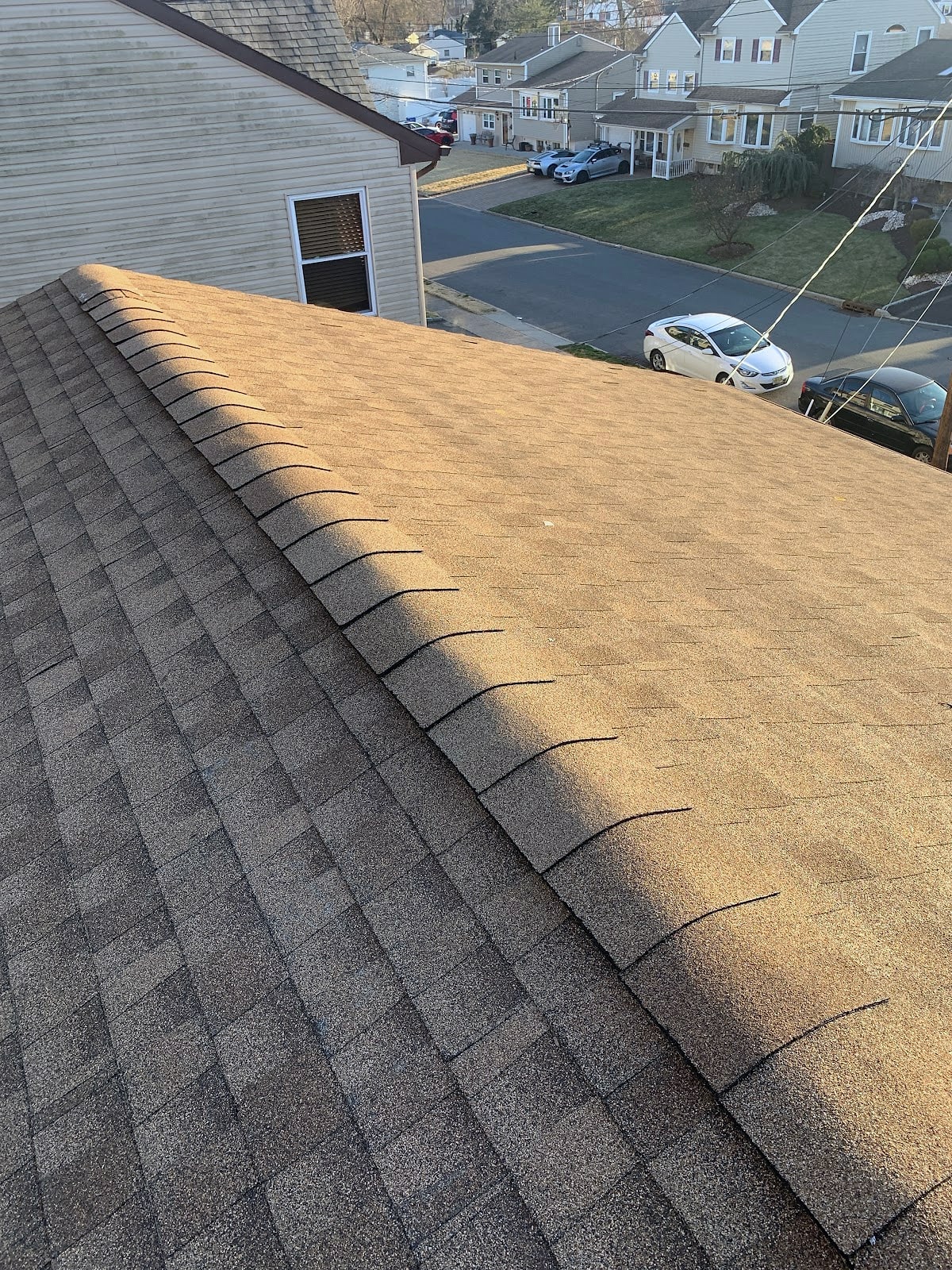 Tan asphalt shingle roof ridge with street and cars below